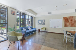 Interior Clubhouse, Community whiteboard, blue couch 2 lounge chairs in front of window, contemporary art on walls, concrete floors.