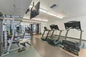 Interior Fitness Center, Multiple weightlifting machines, 3 treadmills, floor mats, mirrored wall, tile flooring, tv above treadmill area.