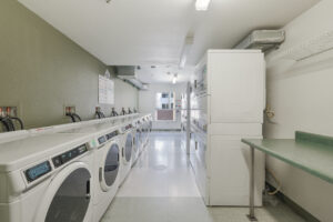 Laundry Facilities, 8 washeres 8 dryers, laminate countertop, rack for clothes hanging, clothes folding table, tile floor, 1 green wall, the rest white walls.